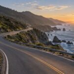 A winding coastal road protected by guardrails as it continues toward sunrise